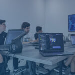 A diverse group of developers, including individuals of different genders and races, seated around an office table, watching a screen.